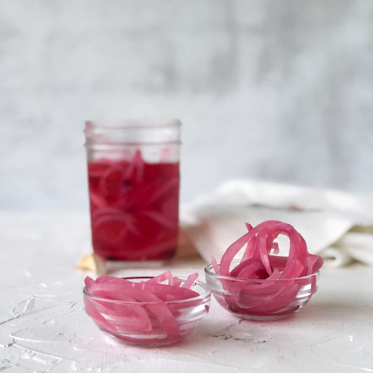 Pickled red onions in two small bowls and canning jar in background.