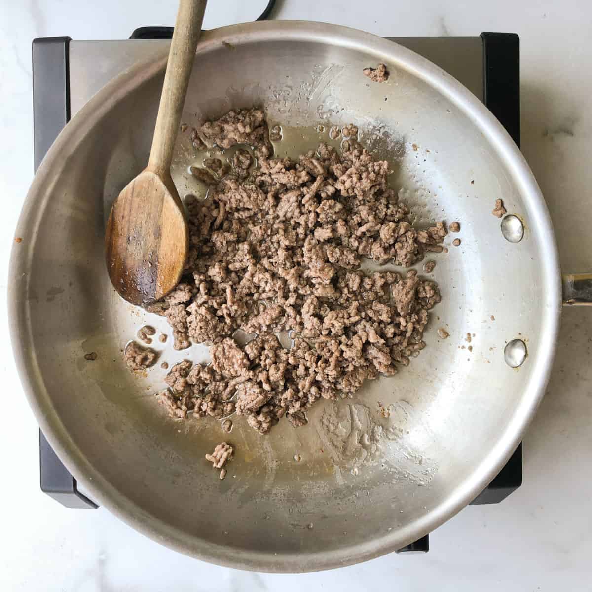 Ground beef cooking in a stainless steel skillet.