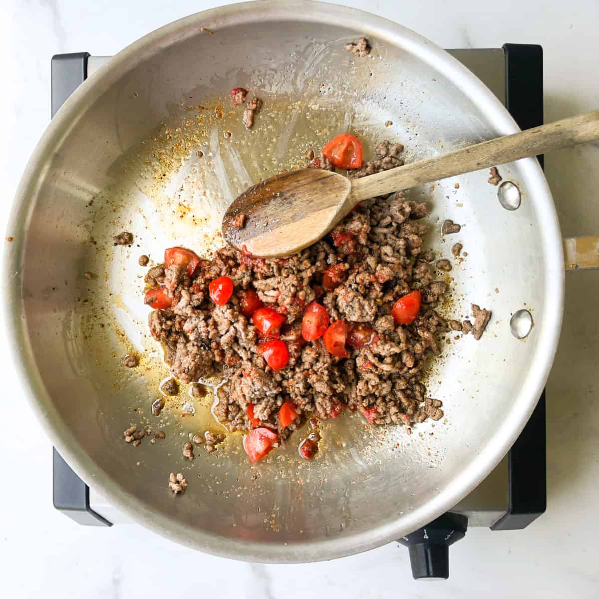 Seasoned ground beef with fresh tomatoes in skillet.