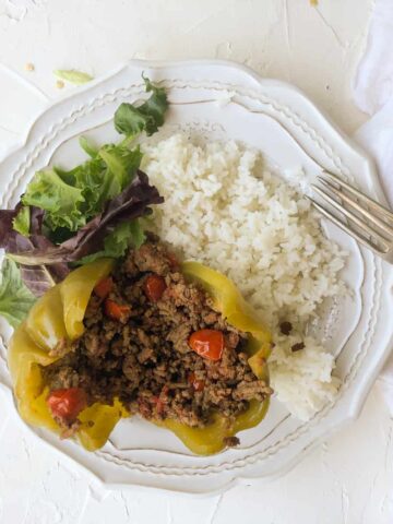 Stuffed green bellpepper with rice and salad on white plate.