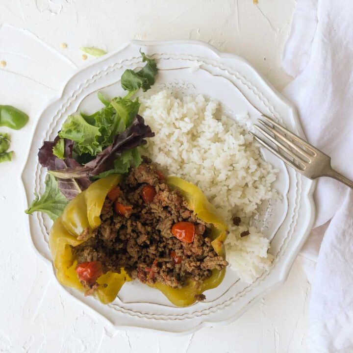 Stuffed green bellpepper with rice and salad on white plate.