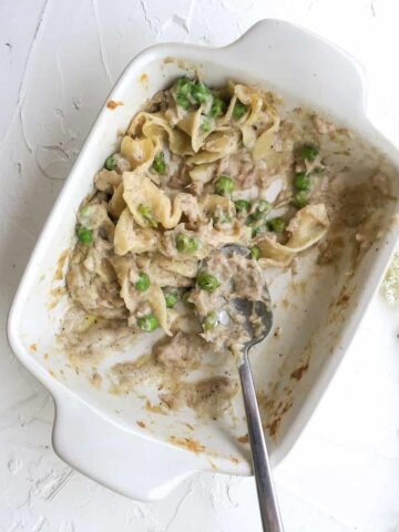 Tuna casserole in small white baking dish with serving spoon.