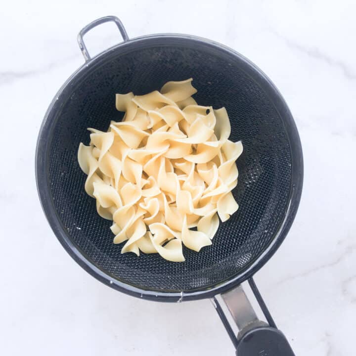 Cooked egg noodles draining in mesh strainer.