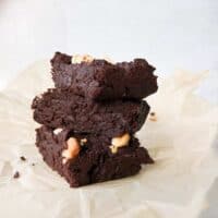Stack of homemade chocolate brownies with white chocolate chips on parchment paper.