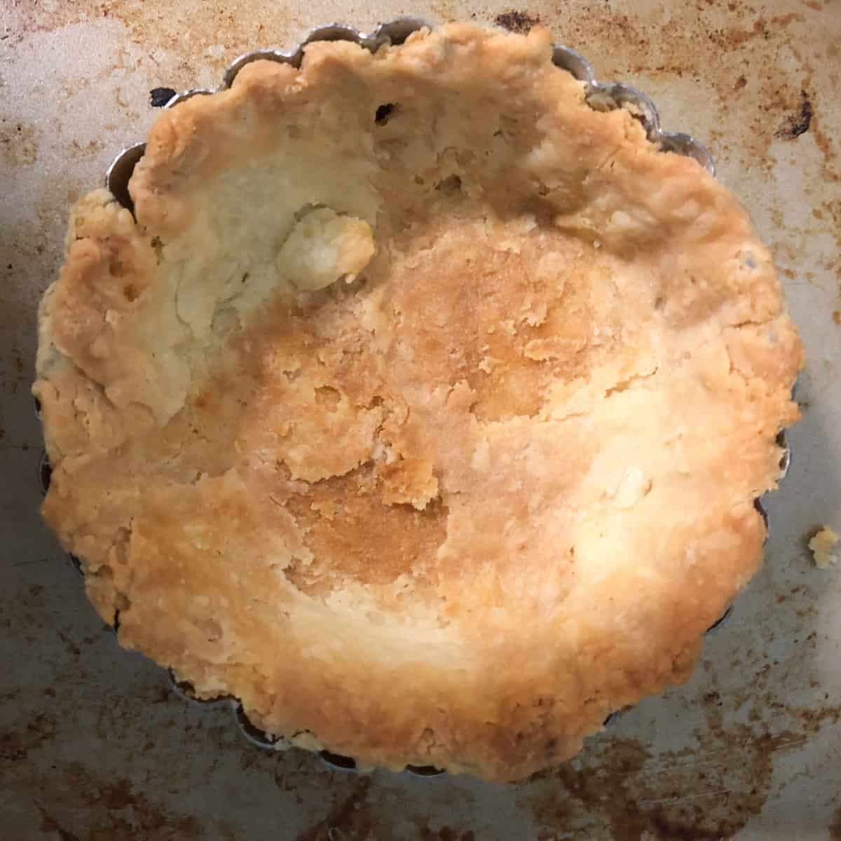 A partially baked, uneven quiche for one crust rests in a fluted tart pan on a stained baking sheet.