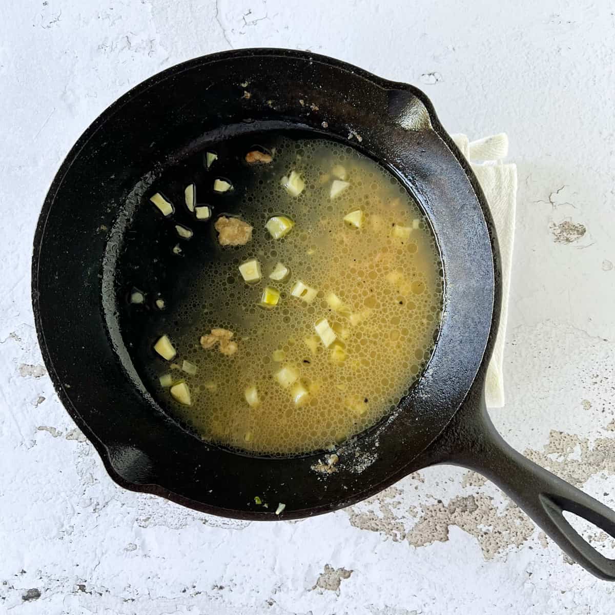 Chciken broth, lemon juice, and garlic simmering in a small cast iron skillet.