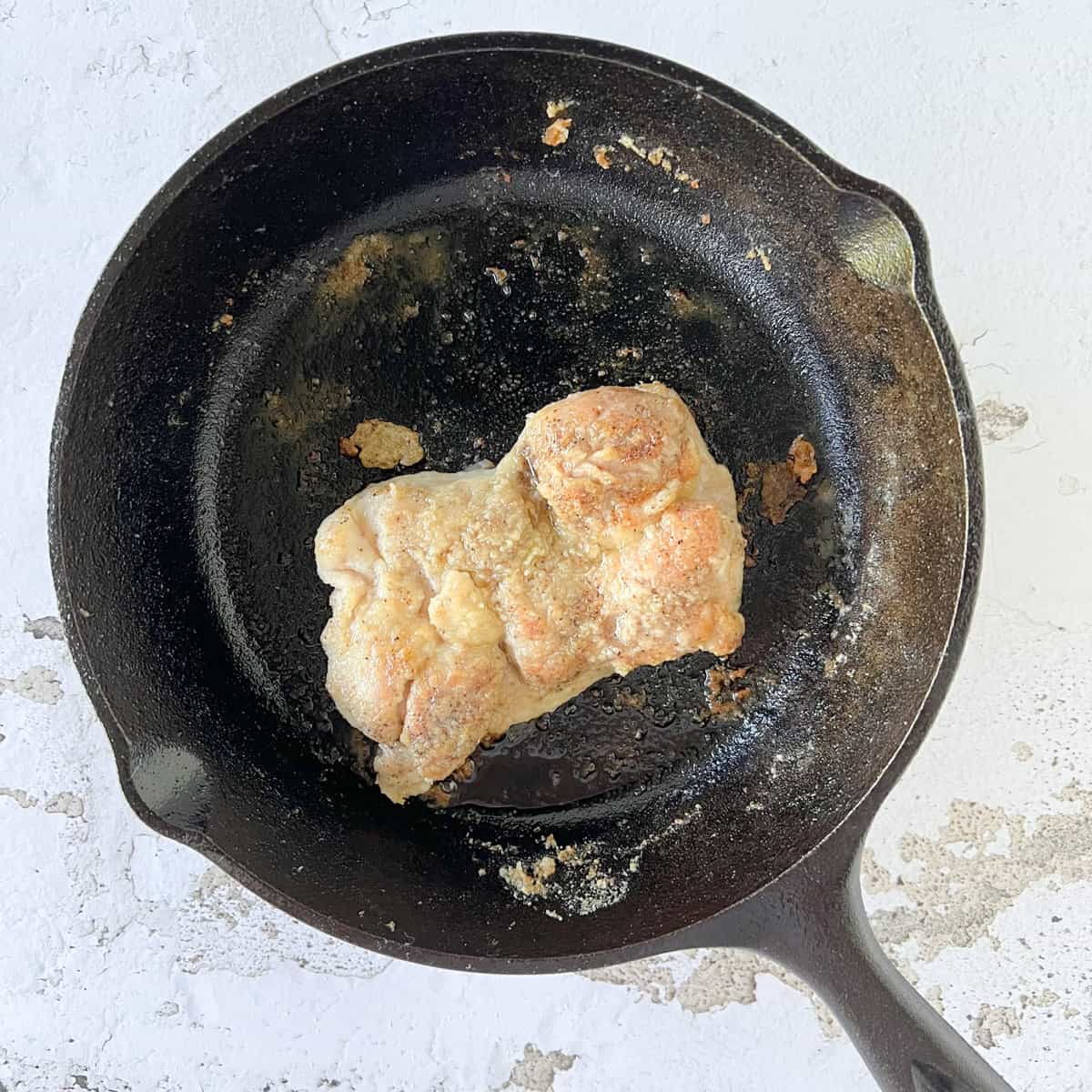 Chciken thigh browning in small cast iron skillet.