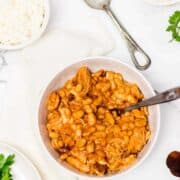 Bowl of stew with beans and chicken on table with spooon and bowl of rice.