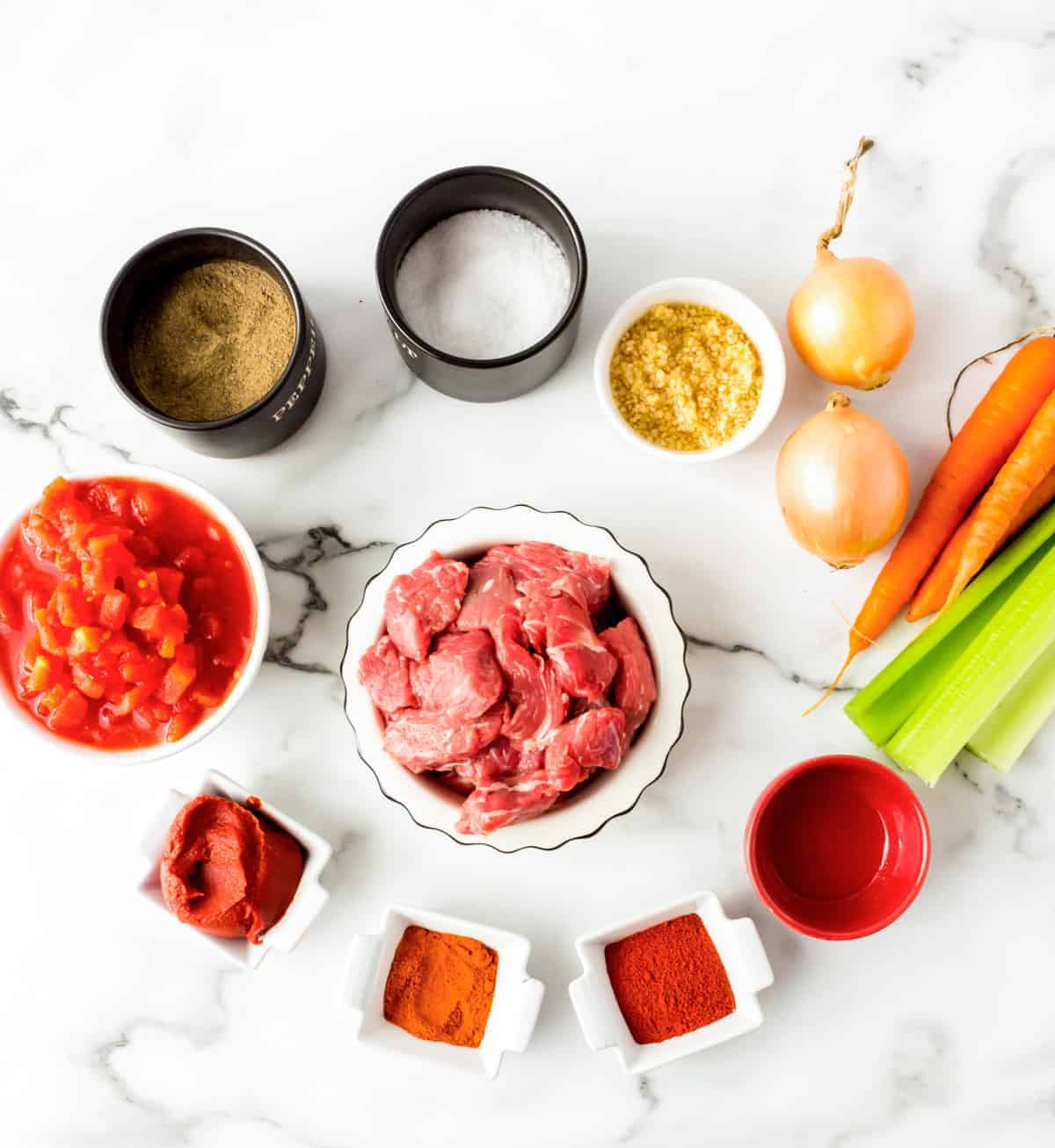 Stew meat, vegetables and seasoning measured in small bowls on marble counter.