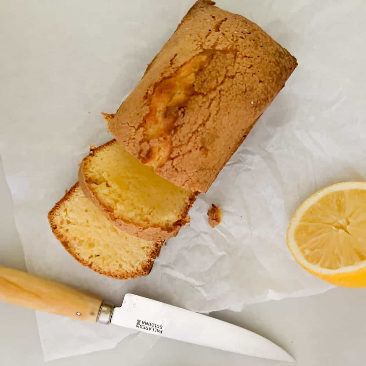 Small pound cake slices with half lemon and knife on parchment paper.
