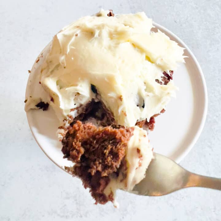 bite of cake on fork over a small frosted cake in a ramekin.