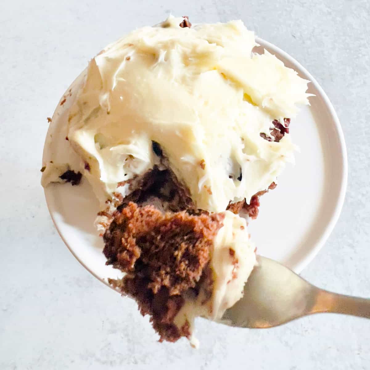 Bite of cake on fork over a small frosted cake in a ramekin.