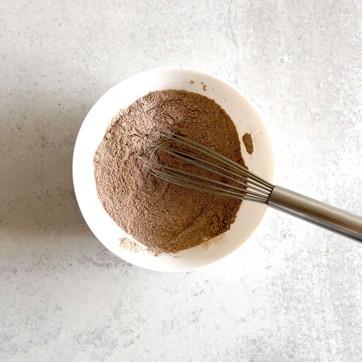 dry ingredients for small cake in white round dish with a mini whisk.