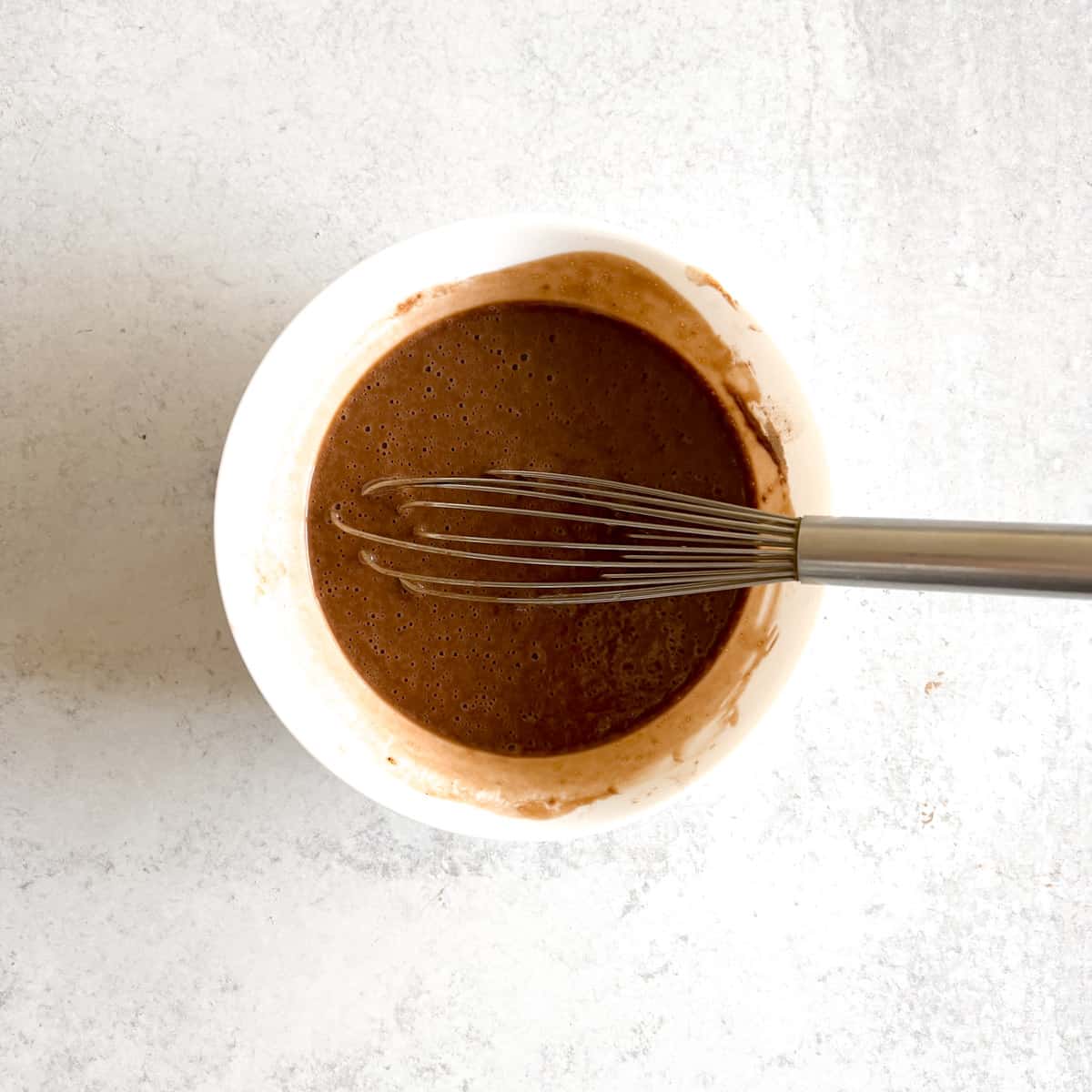 Eggless chocolate cake batter in small round baking dish.
	
