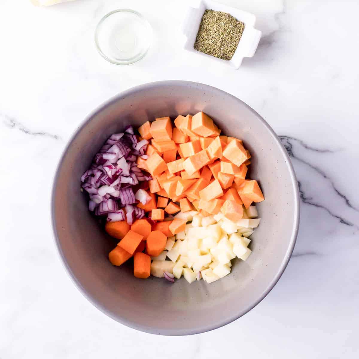 Bowl of diced potatoes, carrots,and onion with spices in small square pinch bow.