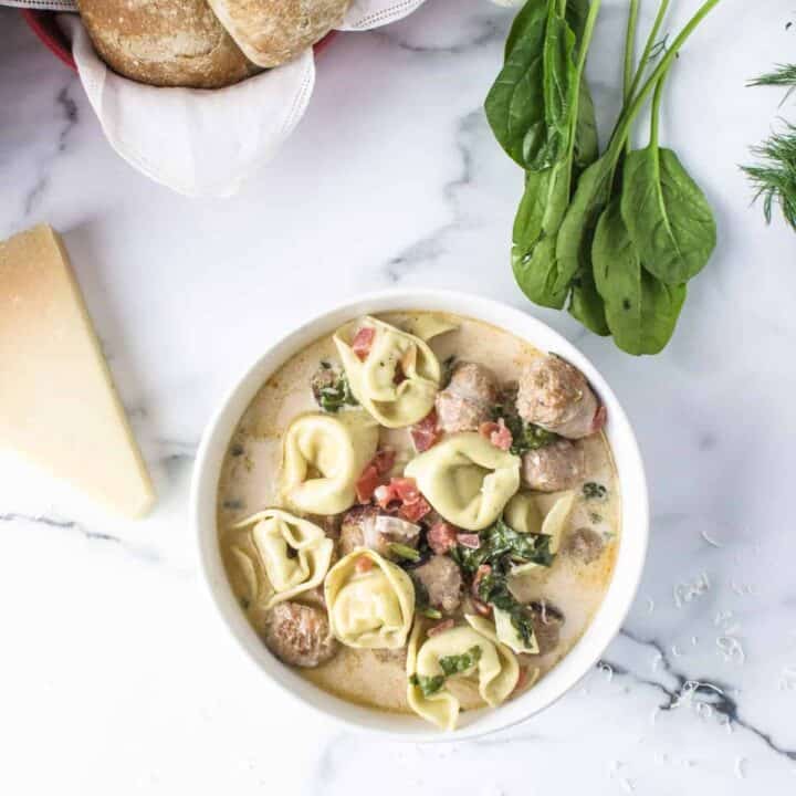 Tortellini stew in a white bowl with fresh spinach on table