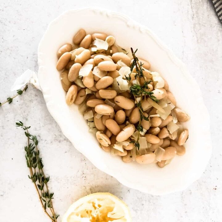 Cooked white beans on oval white plate.