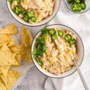 Two bowls of white chicken chili topped with chilantro and green chiles with tortiall chips on table.