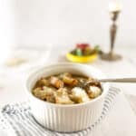 Bowl of french onion soup on striped napkin with candlestick in background.