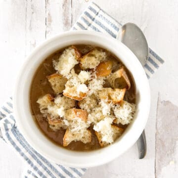 French onion soup topped with croutons in a round white bowl.