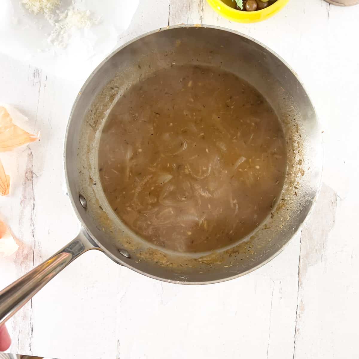Onions and broth cooking in a stainless steel saucepan.