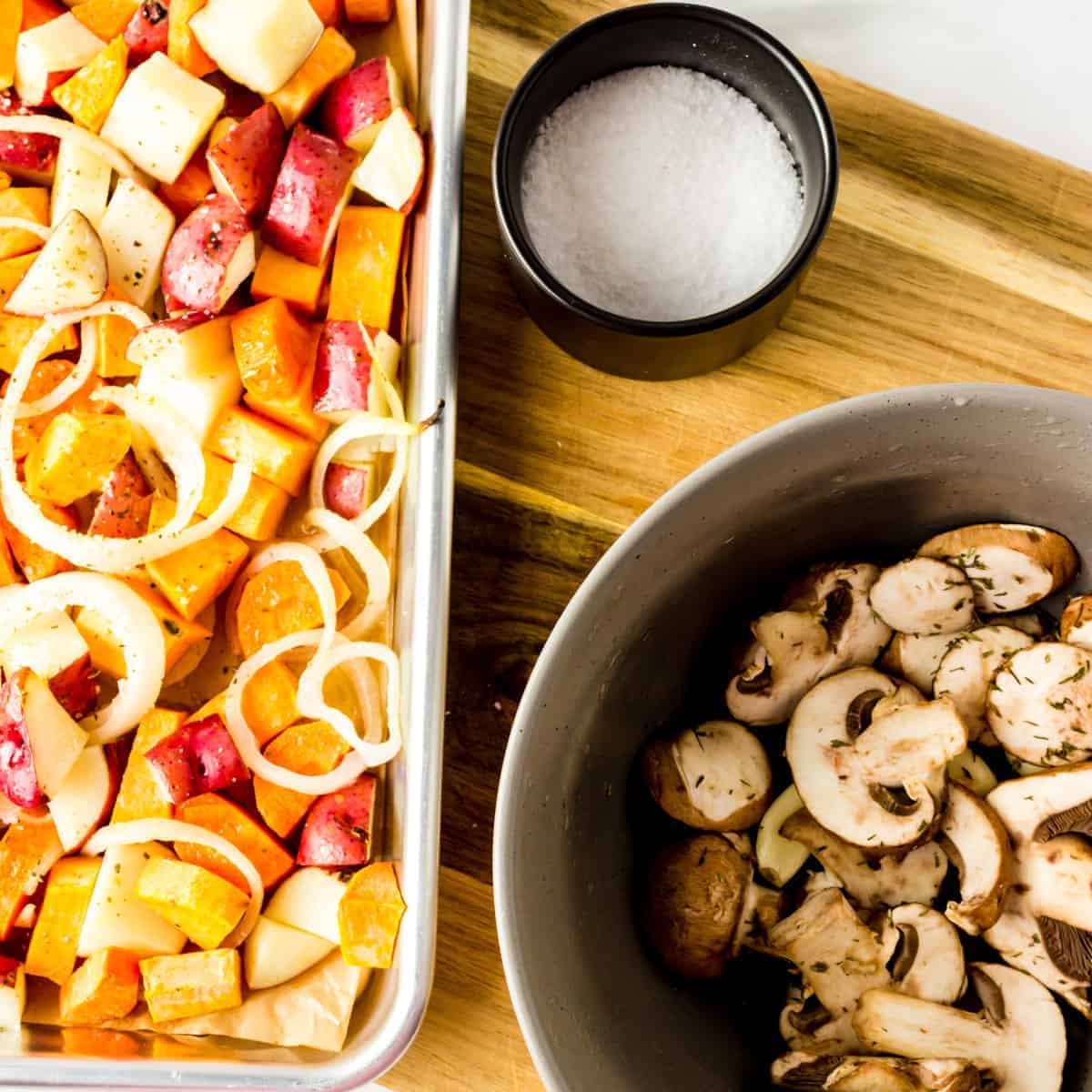 Pan of roasted vegetable next to bowl of mushrooms.