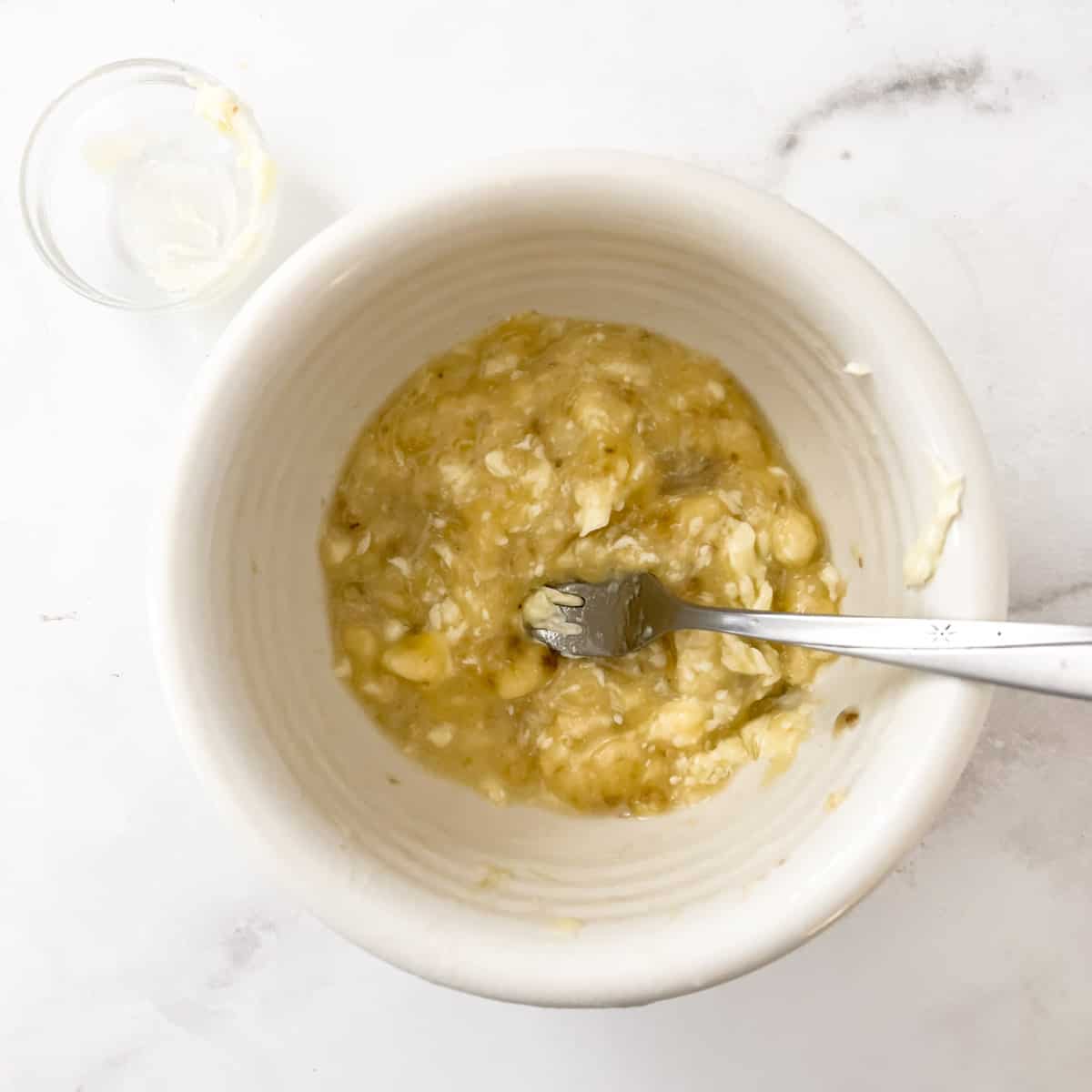 Mashed banana with water and butter in small bowl.