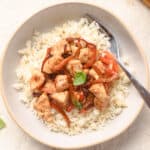 Chicken and red peppers with basil served over rice on plate.