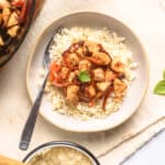 Chicken and red peppers with basil served over rice on plate with side of rice on table.
