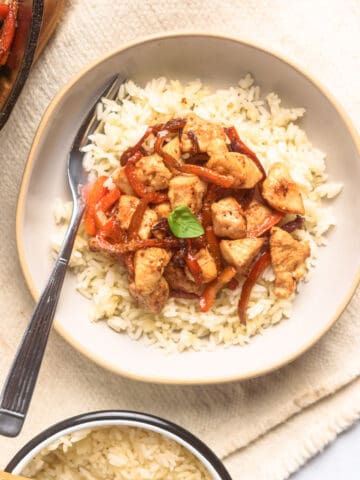 Chicken and red peppers with basil served over rice on plate with side of rice on table.