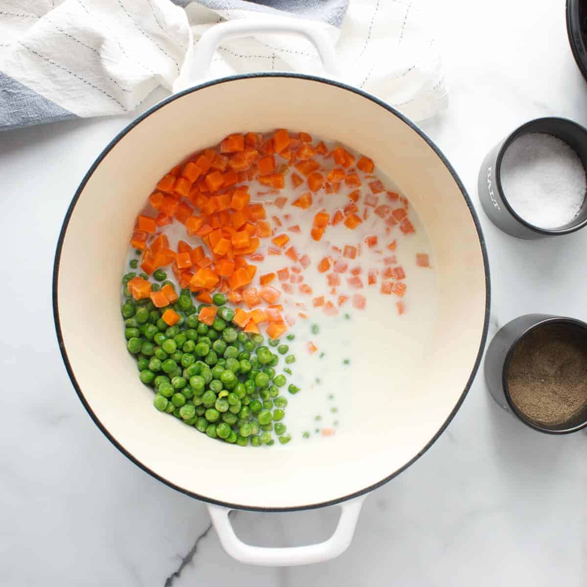 Carrots, peas, and chicken stock in white dutch oven.