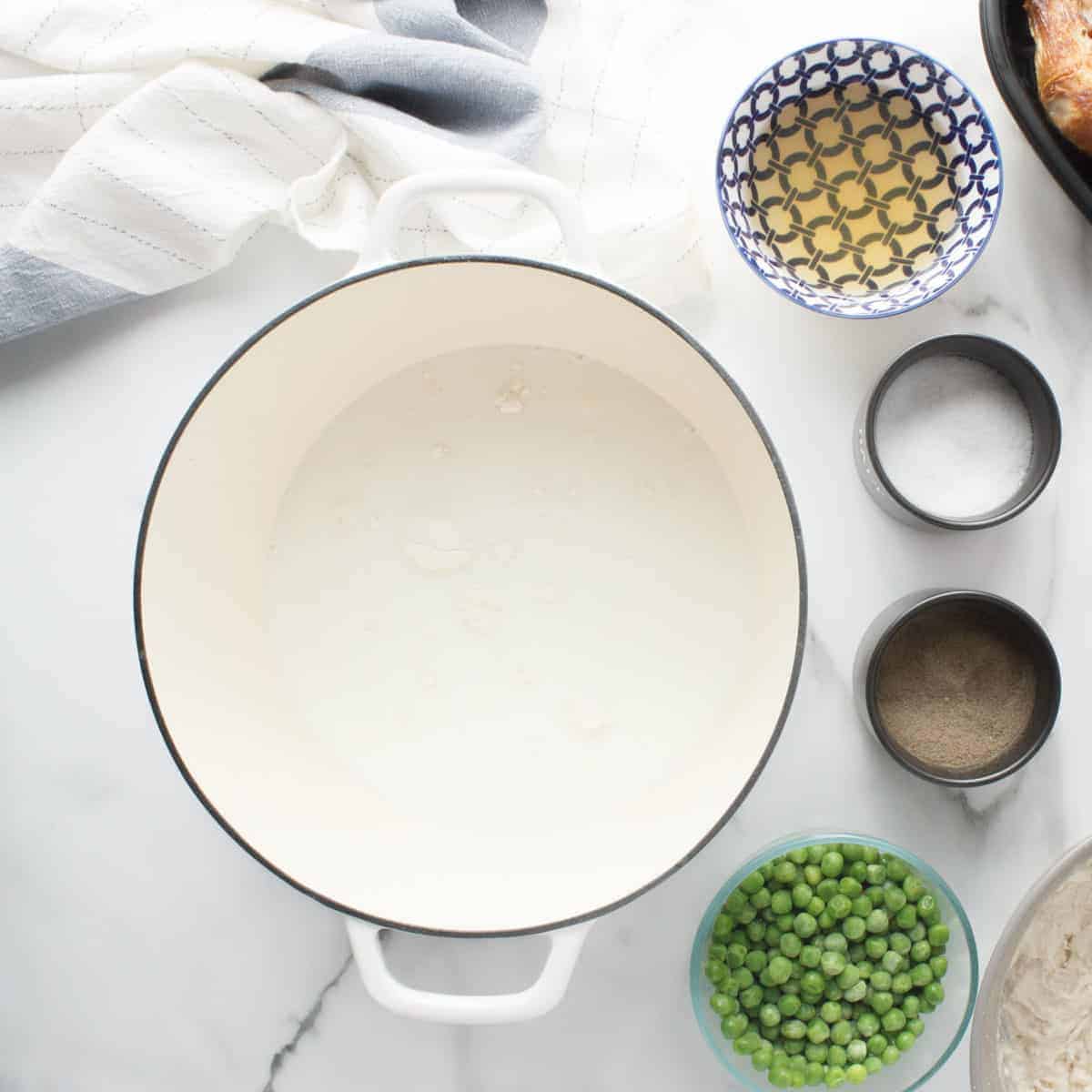 Milk in a white dutch oven with peas on table.
