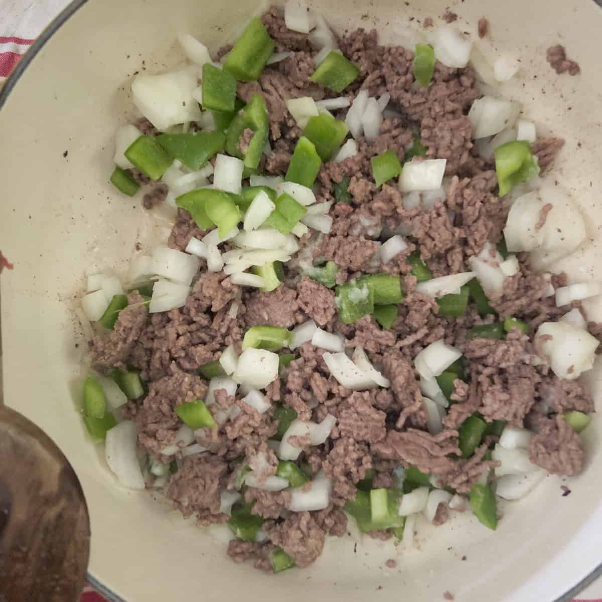 Cooked ground beef with onions and green peppers in dutch oven.