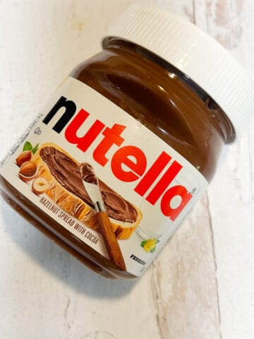 Jar of Nutella spread on white washed wood surface.