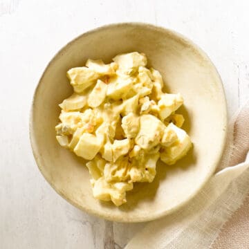 Small bowl of egg salad with white plate of bread in corner.