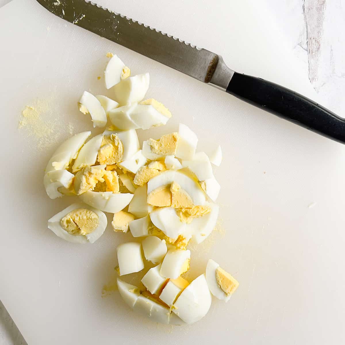 Chopped hard boiled egg on white cutting board.