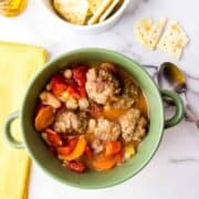 Green bowl filled with meatball stew next to yellow napking and sppon on marble counter.