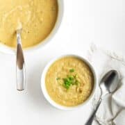 White bowl of parsnip leek soup with soup spoon and napkin on white table surface.