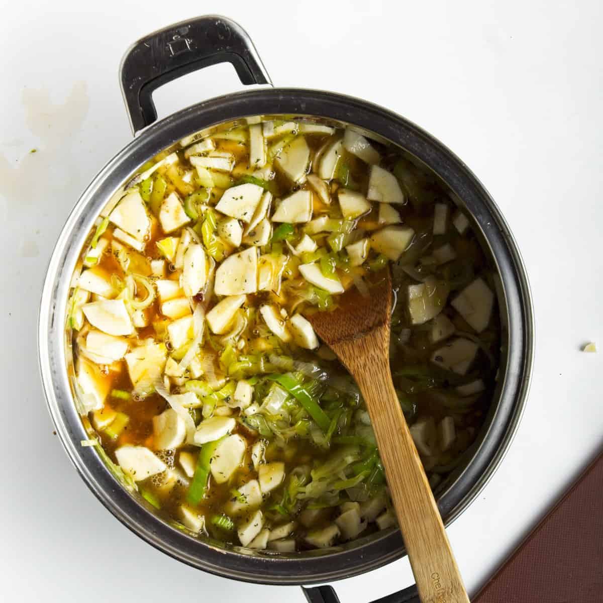 Parsnip and leek soup ingredients simmering in saucepan with wooden spoon.