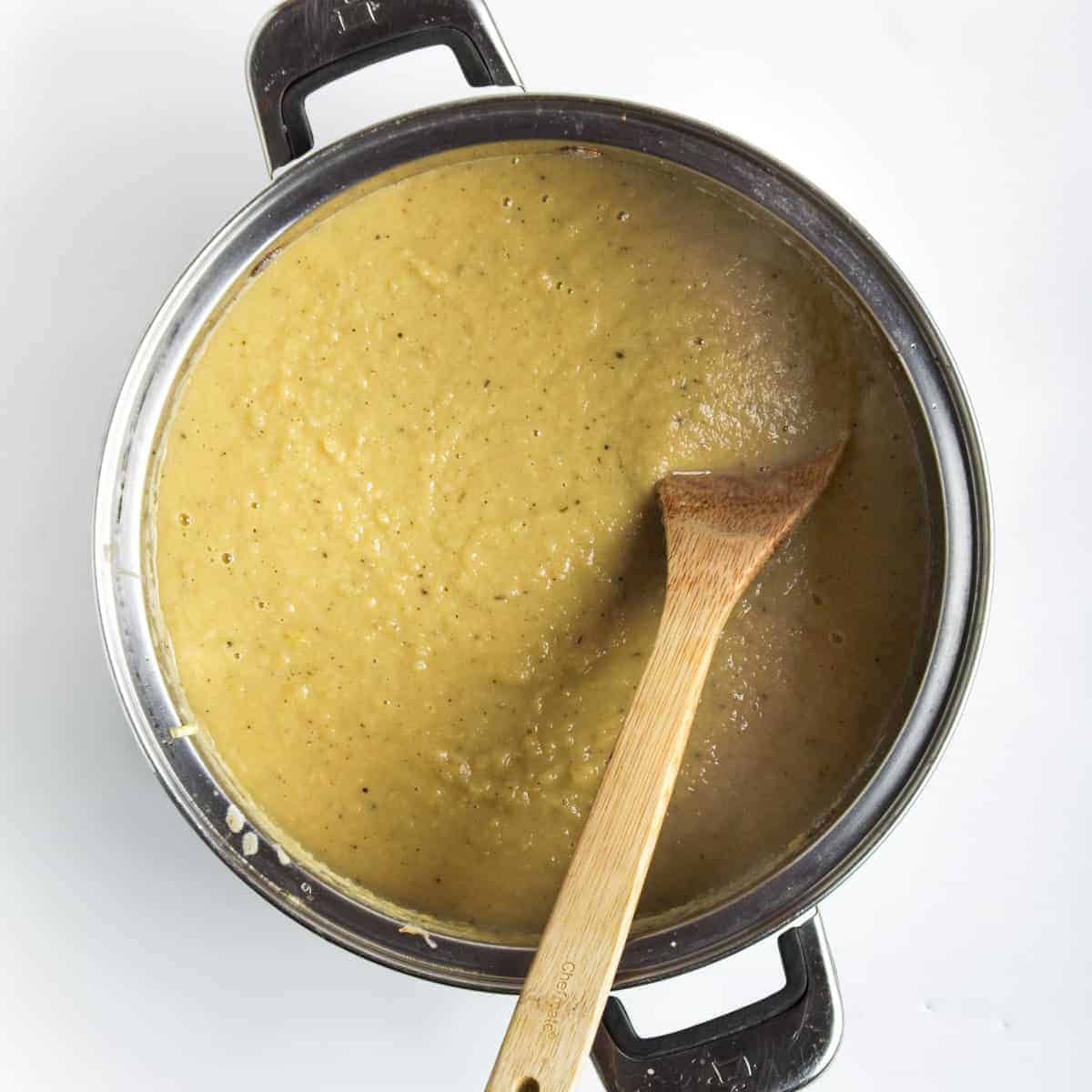 Saucepan with creamy parsnip leek soup and wooden spoon.