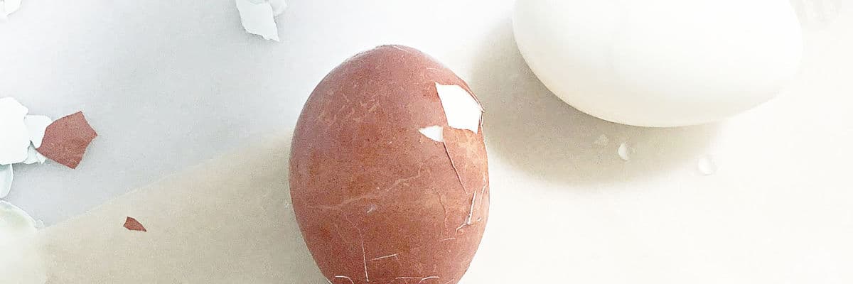Two eggs, one in brown shell partially peeled and one peeled egg.