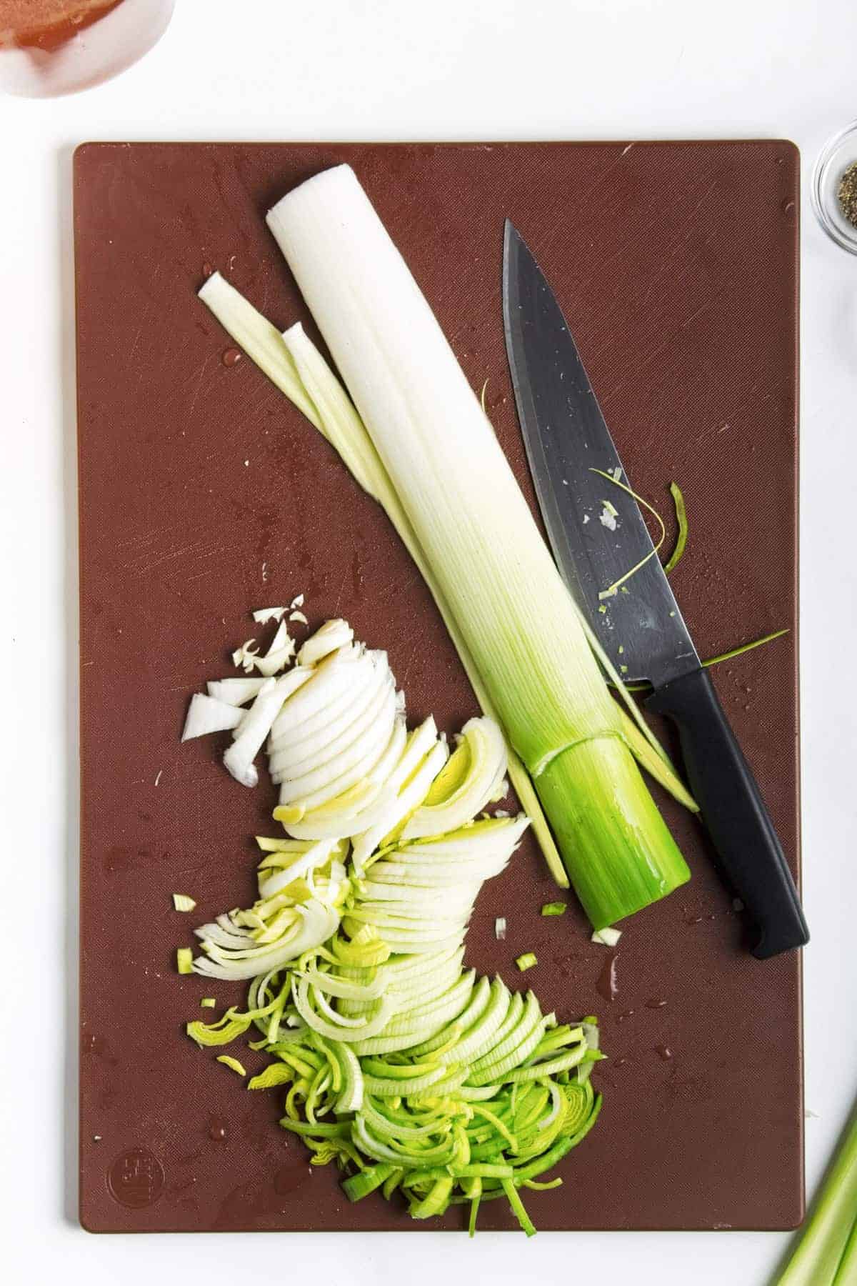Fresh leek partially sliced on cutting board with black handle knife.