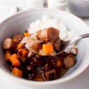 Bowl of black bean stew with carrots and rice on side.