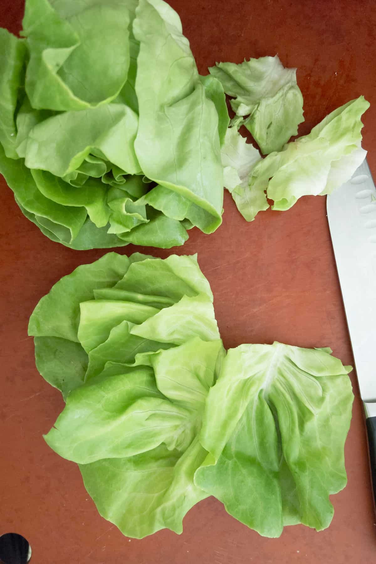 Butterhead lettuce leaves on cutting board with chefs knife on side.