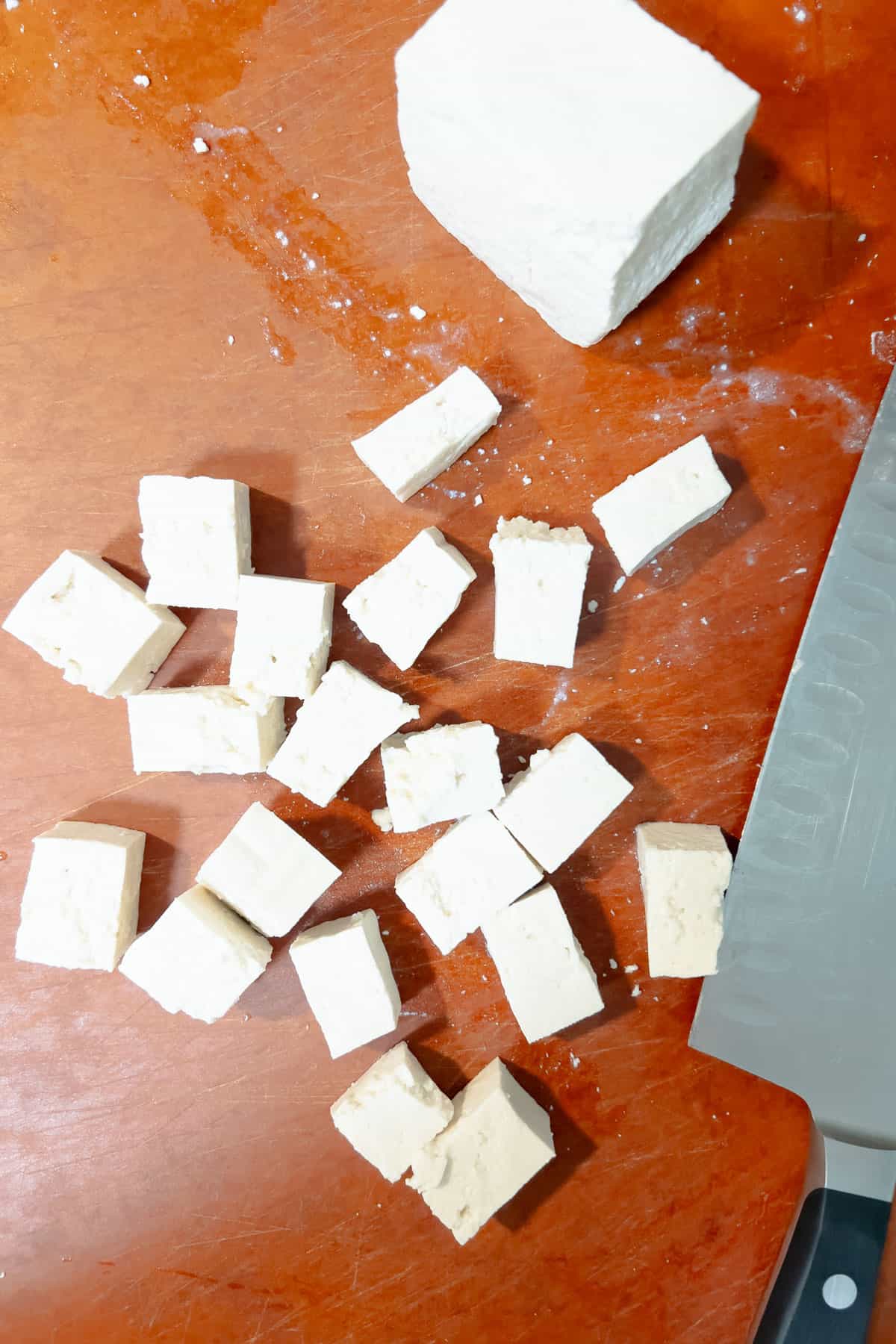 Diced tofu cubes on cutting board with chefs knife on side.