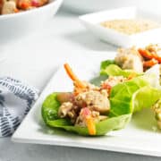 Tofu filling in lettuce leaves on square white plate.