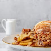 Close-up of a mini apple crisp topped with ice cream and cinnamon, with a small milk jug in the background.