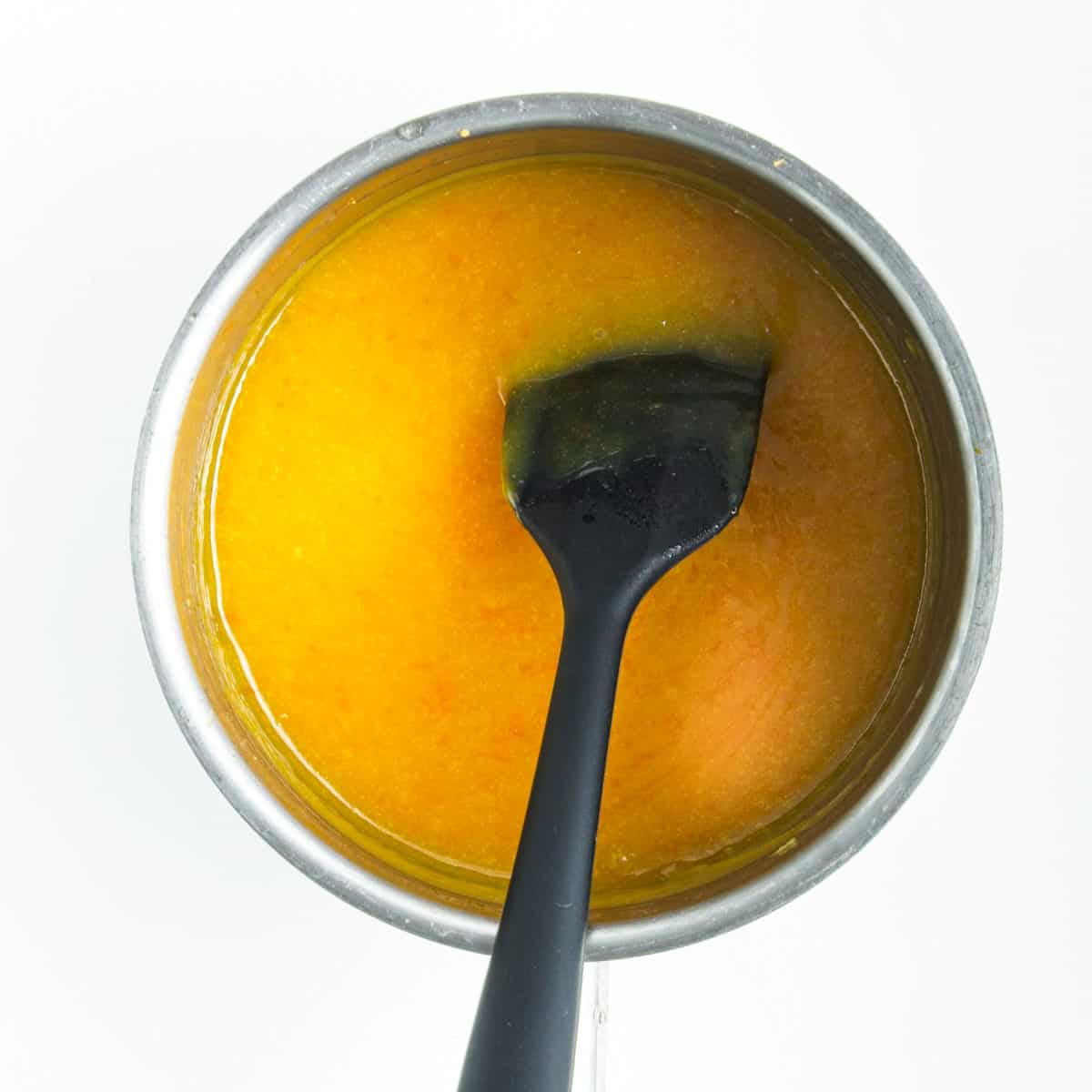 Orange curd cooking is saucepan and black flat spoon.