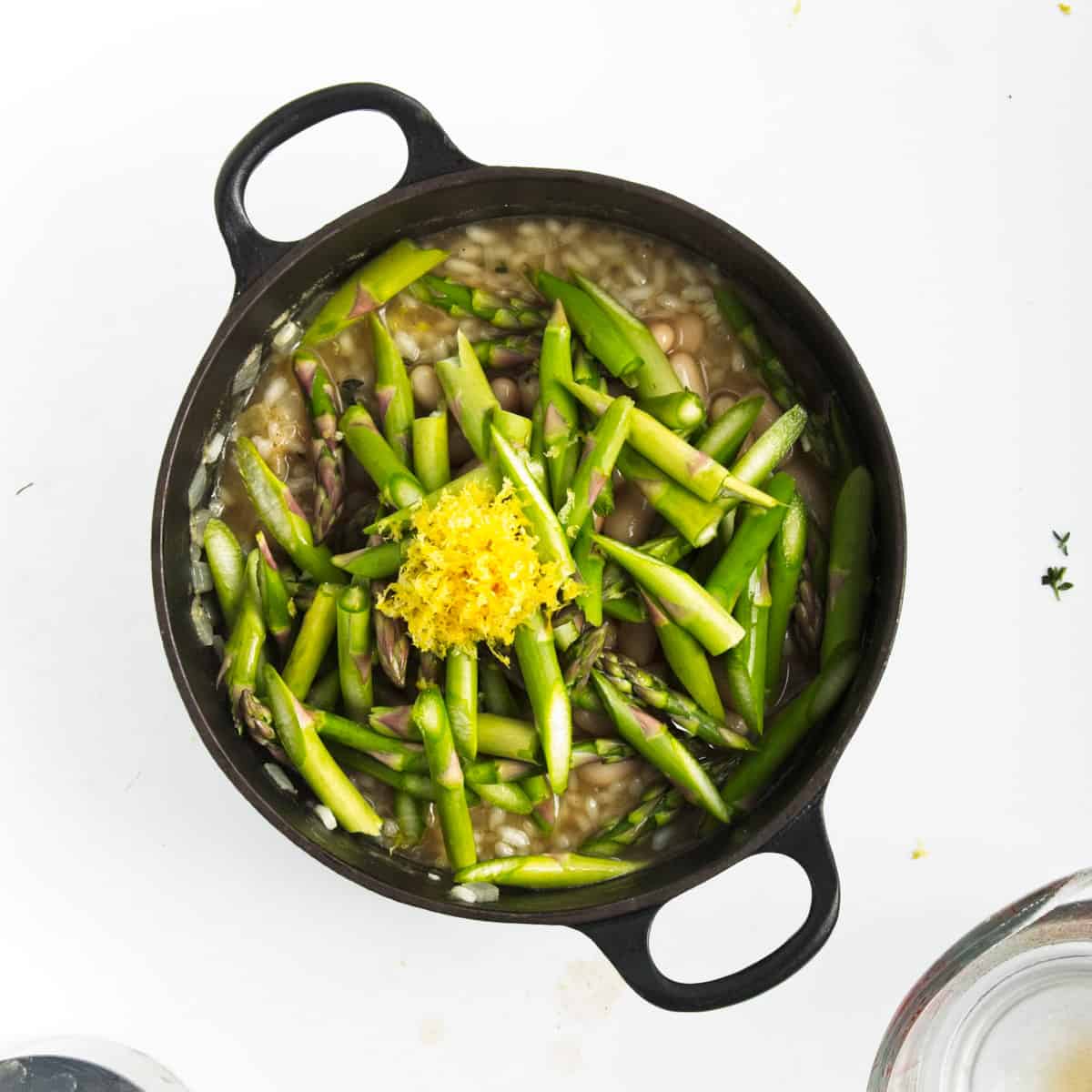 White bean risotto in saucepan and topped with asparagus and lemon zest.