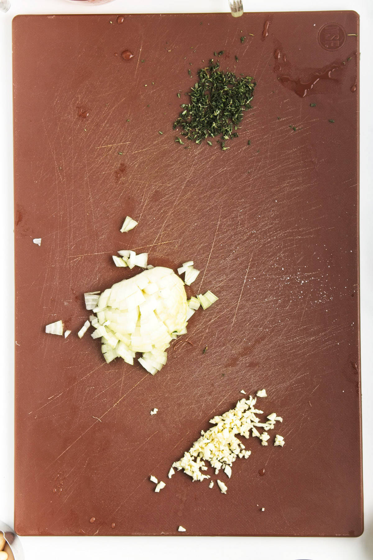Onion, garlic and thyme chopped on a cutting board.